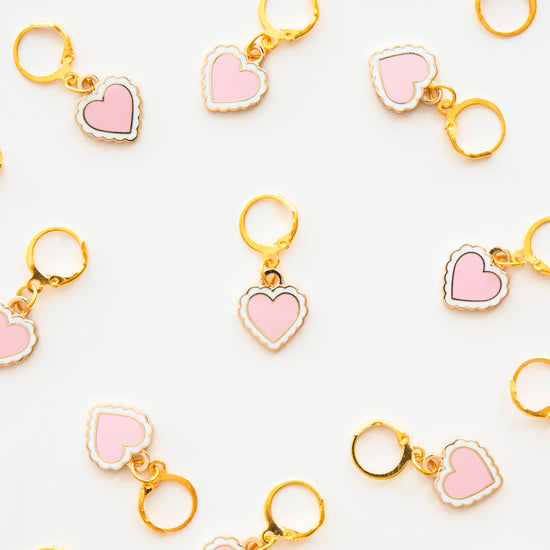 Heart-shaped stitch marker with pink hearts and gold metal on a white background