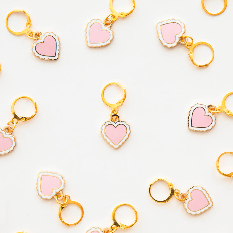 Heart-shaped stitch marker with pink hearts and gold metal on a white background