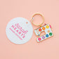 Enamel keychain with sewing machine design and 'Sarah Hearts' branding on a pink background